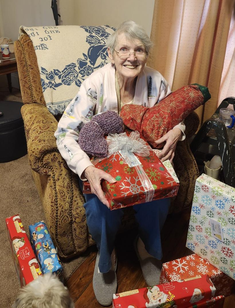 Elder Orphan Care friend smiling and covered in Christmas gifts